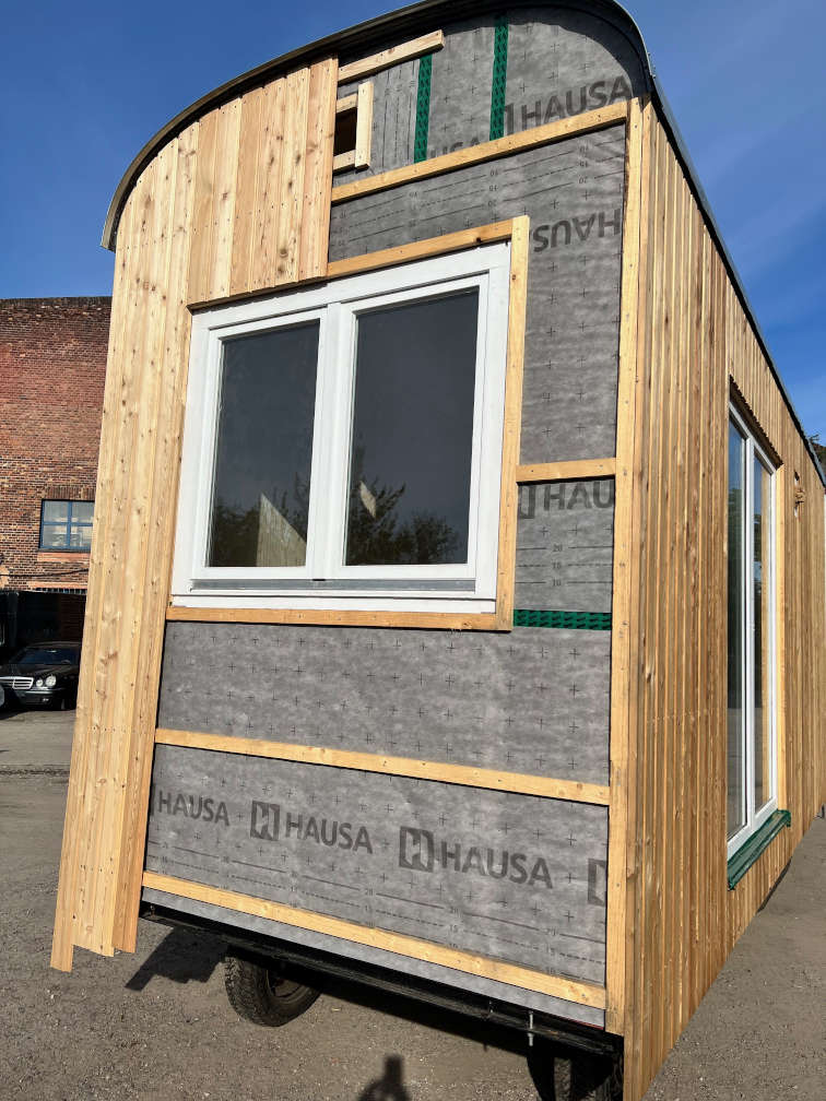 Es ist die Giebelansicht eines »Tiny Houses« zu sehen – sowohl mit und ohne Verkleidung. Die Dämmung wird so an einigen Stellen sichtbar.