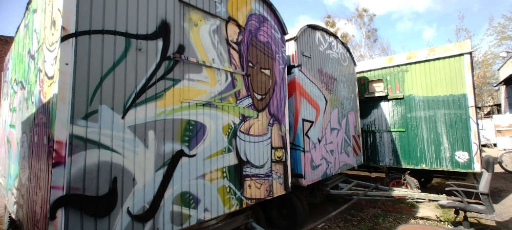 Das Bild zeigt drei alte, mit Farbe bunt bemalte, Bauwagen. 